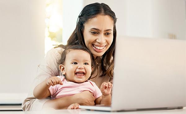 Young mother holding her baby and using a laptop